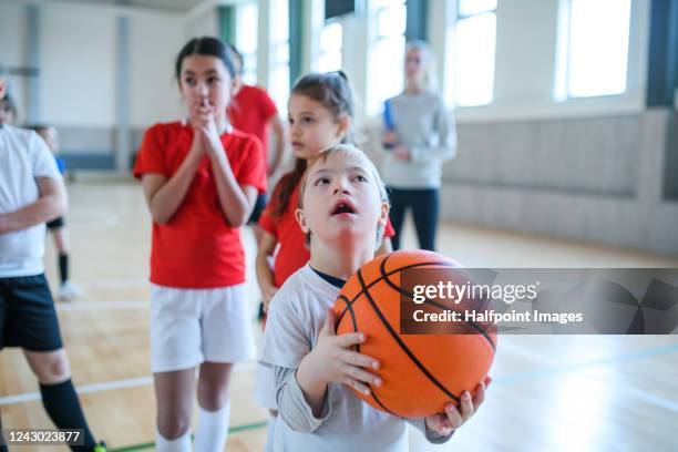 down syndrome boy with pupils exercising indoors in gym class, playing basketball. - school sports bildbanksfoton och bilder