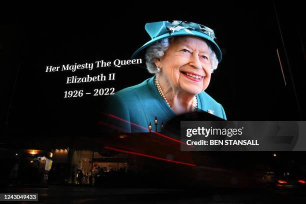 Members of the public stop in the rain to study a huge picture of Britain's Queen Elizabeth II displayed at Piccadilly Circus in central London on...