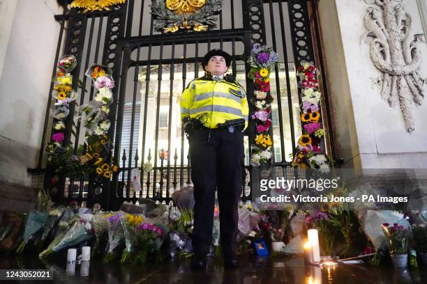 Police officer stands amongst floral tributes left outside Buckingham Palace in central London, following the announcement of the death of Queen...