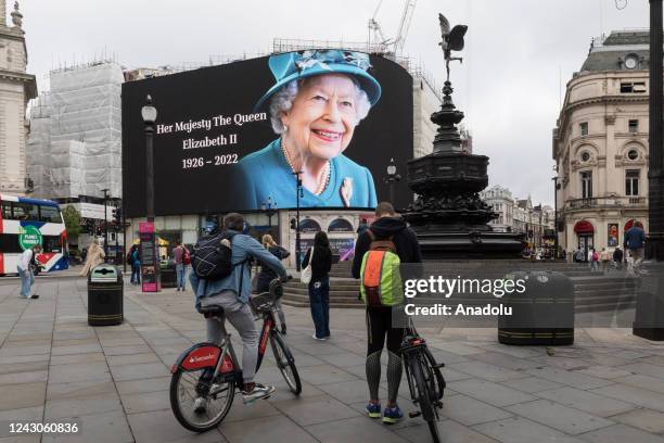 People stop to pay their respects as a tribute to Queen Elizabeth II is displayed on the large screen in Piccadilly Circus on the first day of...