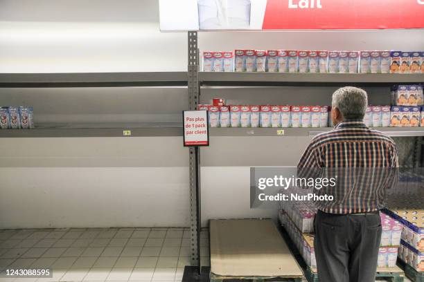 Man reads a poster that reads, no more than one packet per customer, and that is displayed on an almost empty shelve of milk in a supermarket in...