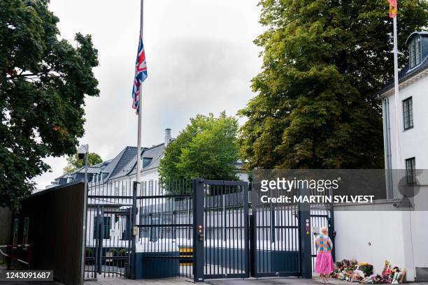 The British flag flies at half-mast as a wellwisher stands by flowers in front at the British Embassy in Copenhagen, Denmark, on September 10 to pay...