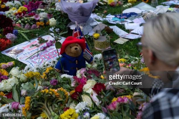 Woman photographs a Paddington Bear toy left among flowers and tributes to Queen Elizabeth II in Green Park on September 10, 2022 in London, United...