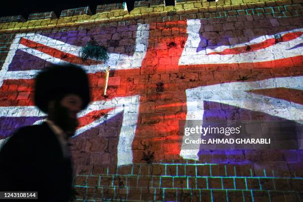 An ultra-Orthodox Jewish man walks past a projection of the British Union Jack flag displayed on the walls of the old city of Jerusalem on September...