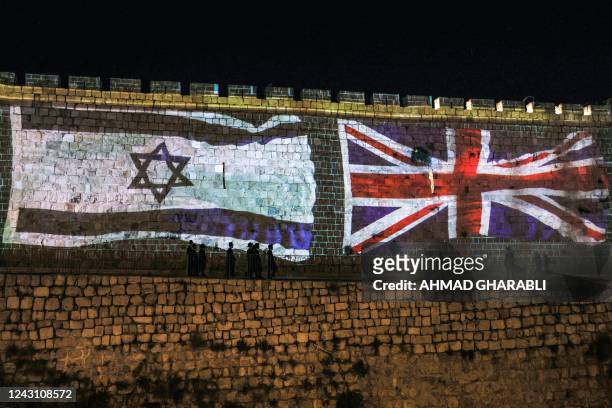 People walk past projections of the flags of Israel and the British Union Jack displayed on the walls of the old city of Jerusalem on September 10...