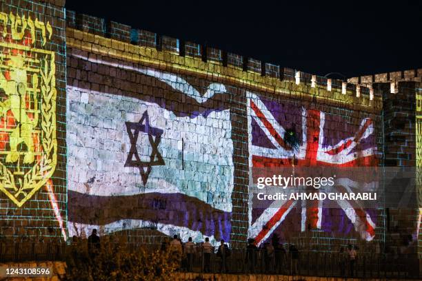 People walk past projections of the emblem of the city of Jerusalem and the flags of Israel and the British Union Jack, displayed on the walls of the...