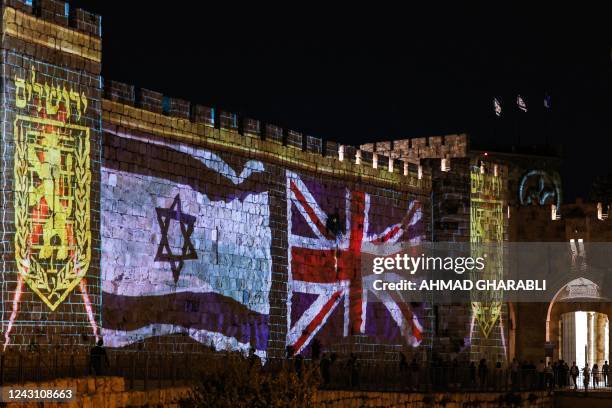 People walk past projections of the emblem of the city of Jerusalem and the flags of Israel and the British Union Jack, displayed on the walls of the...