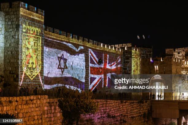 People walk past projections of the emblem of the city of Jerusalem and the flags of Israel and the British Union Jack, displayed on the walls of the...