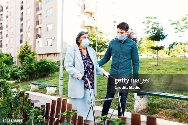 young man helping senior woman walking in the street - volunteer aged care stock pictures, royalty-free photos & images