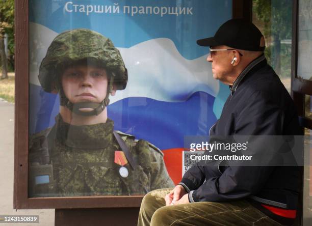 Man looks at a poster at a bus stop featuring a portrait of Alexander Noskov, a Russian ensign participating in the military invasion of Ukraine, on...