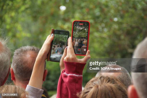 People hold up their mobile phones to ty and get a shot outside the gates of Clarence House following a hint that King Charles would be driven by...