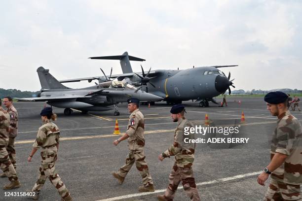 French Air Force personnel walk past a Dassault Rafale multirole combat aircraft and an Airbus A400M airlifter on the apron of the Halim...