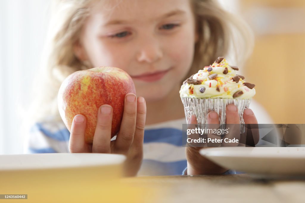 Girl choosing between an apple and a cake