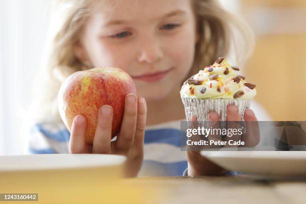 girl choosing between an apple and a cake - child holding apples stockfoto's en -beelden