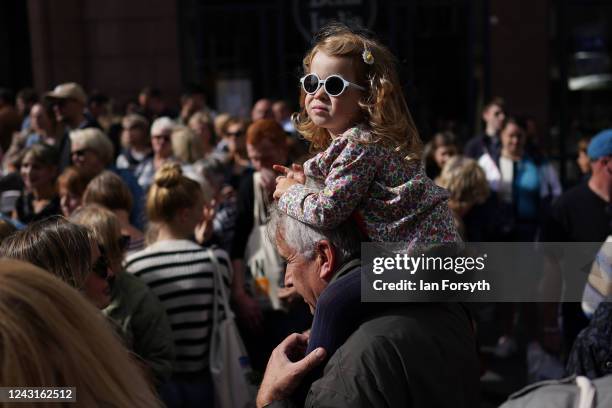 Young girl sits on the shoulders of a man as they wait to view the cortege carrying the coffin of the late Queen Elizabeth II on September 12, 2022...