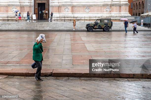 Rain in Piazza Maggiore in Bologna, an elderly lady covers herself with a bag to avoid the rain. In Bologna, Italy in September 2022.