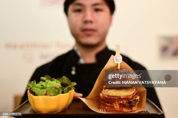 This photo taken on August 30 shows Pooripat Thiapairat, owner of 'Bounce Burger', posing with a plate of "Cricket-burger" at his restaurant in...