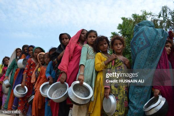 Displaced flood-affected people stand in a queue to receive food being distributed by Saylani Welfare Trust at a makeshift camp in flood-hit Sehwan...