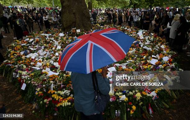 Member of the public shelters from the rain beneath a Union flag-themed umbrella as they look at flowers and tributes left in Green Park in London on...