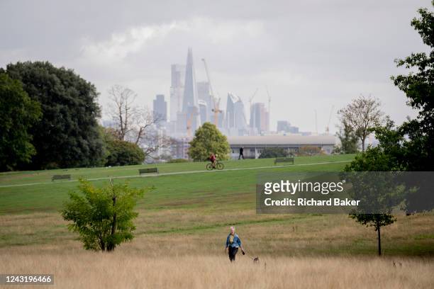 With skyscrapers in the City of London, the capital's financial district, in the distance, a a cyclist pedals uphill, a park user walks alongside and...