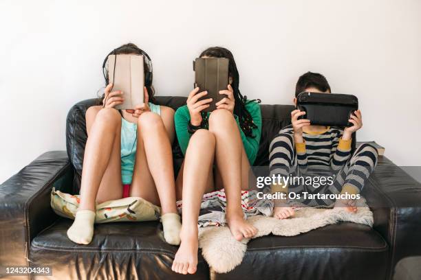 three kids with electronic devices on a sofa - tablet screen home stock-fotos und bilder