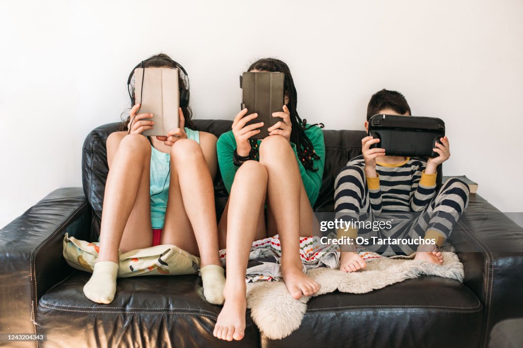 Three kids with electronic devices on a sofa