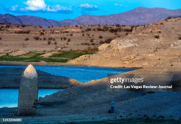 Photographer Mario Tama walks as the late-day light illuminates a boat is stuck straight up along the shoreline as water levels continue to drop at...