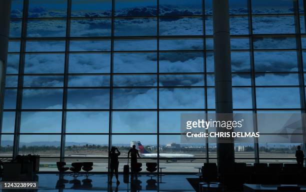 People stand beneath a picture of clouds on a large window as they watch planes take off from the Tom Bradley International terminal at Los Angeles...