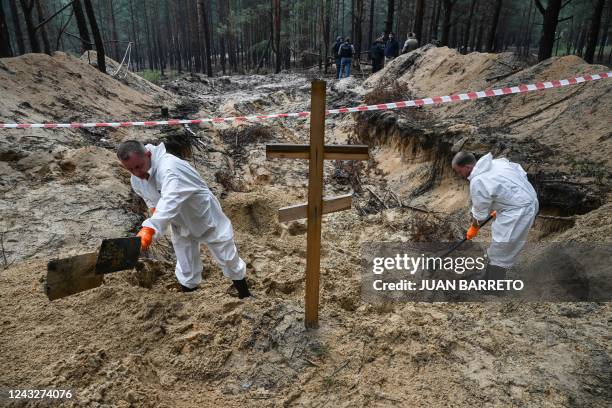 Graphic content / TOPSHOT - Two forensic technicians dig near a cross in a forest on the outskirts of Izyum, eastern Ukraine on September 16, 2022. -...