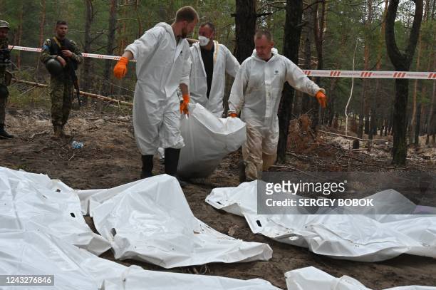 Forensic technicians carry a body bag in a forest on the outskirts of Izyum, eastern Ukraine on September 16, 2022. - Ukraine said on September 16,...