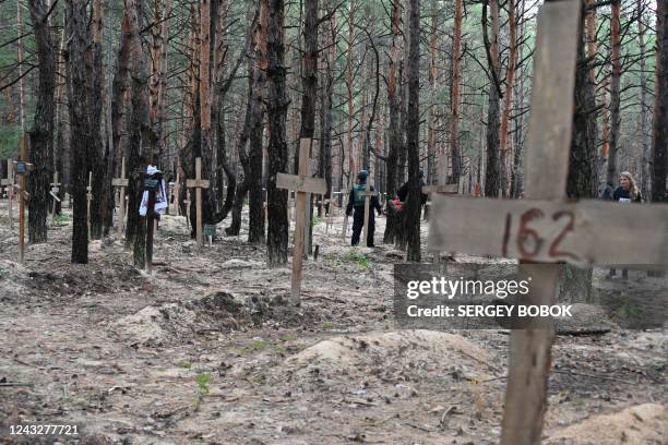 Ukrainian police officers walk among crosses in a forest on the outskirts of Izyum, eastern Ukraine on September 16, 2022. - Ukraine said on...