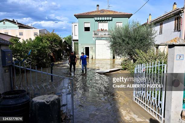 Two men walk in a flooded courtyard following an overnight rain bomb in Pianello di Ostra, Ancona province, on September 16, 2022. - At least ten...