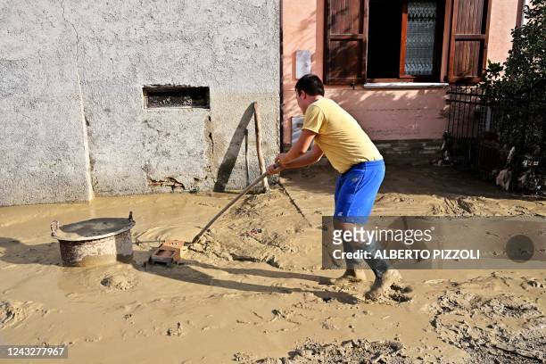 Man cleans a flooded street following an overnight rain bomb in Pianello di Ostra, Ancona province, on September 16, 2022. - At least ten people died...