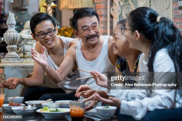 a senior married couple eating dinner with their adult children in their apartment in vietnam - vietnamesischer abstammung stock-fotos und bilder