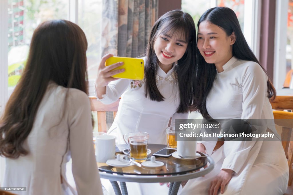 Vietnamese girlfriends in traditional dress having coffee together