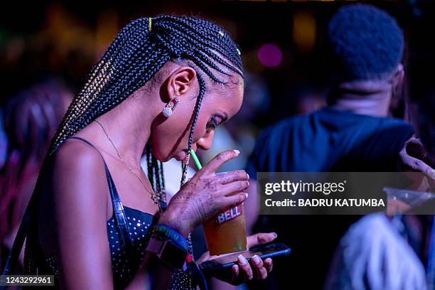 Ugandan Nyege Nyege festival-goer looks on her phone while sipping from a drink at the Itanda Falls on the second day of Nyege Nyege festival, the...