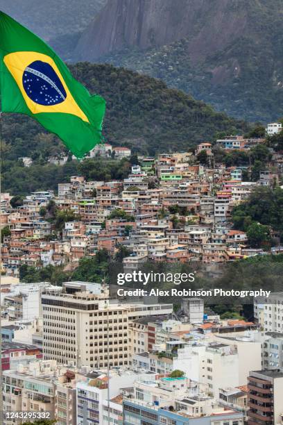 view of a favela slum in rio de janeiro with a brazilian flag flying in the foreground - social inequality ストックフォトと画像