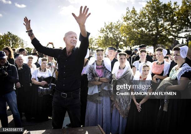 British photographer Jimmy Nelson puts his hands up in the air next to participants in traditional Dutch attire for a group portrait during a meeting...