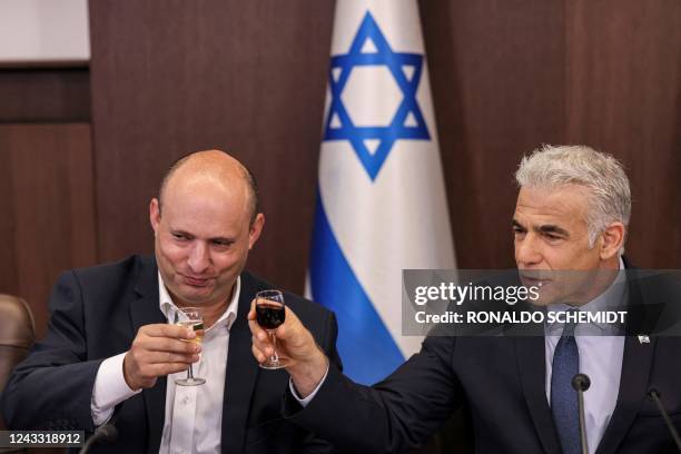 Israel's caretaker Prime Minister Yair Lapid and former prime minister Naftali Bennett toast with small glasses of wine during the weekly cabinet...