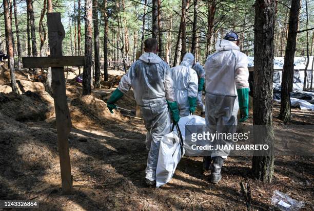 Graphic content / TOPSHOT - Forensic technicians carry a body in a bodybag at the site of a mass grave in a forest on the outskirts of Izyum, eastern...