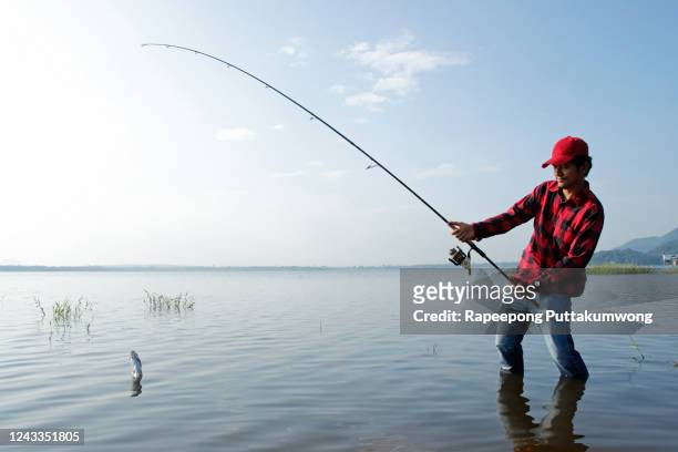 fisherman standing in a lake and catching the fish with fishing rod - fishing reel foto e immagini stock