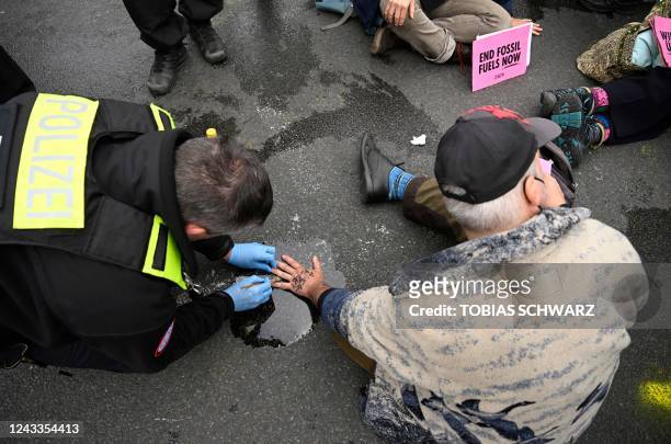Policeman works on the hand of a man who has glued himself on the street as climate activists of the "Last Generation" movement demonstrate against...