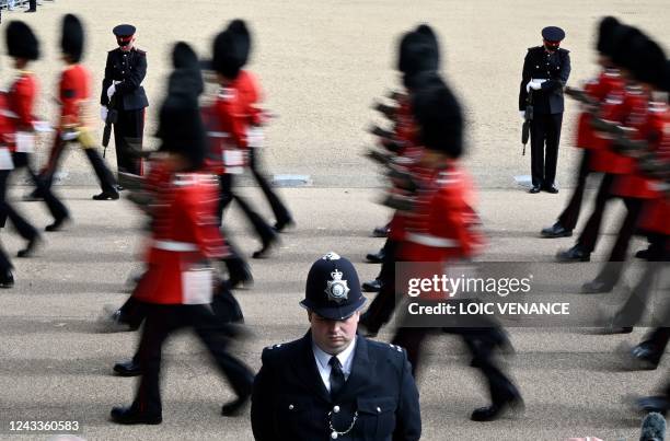 Police officer stands in position as members of the King's Guard march during the Procession of the coffin of Queen Elizabeth II, at Horse Guards, on...