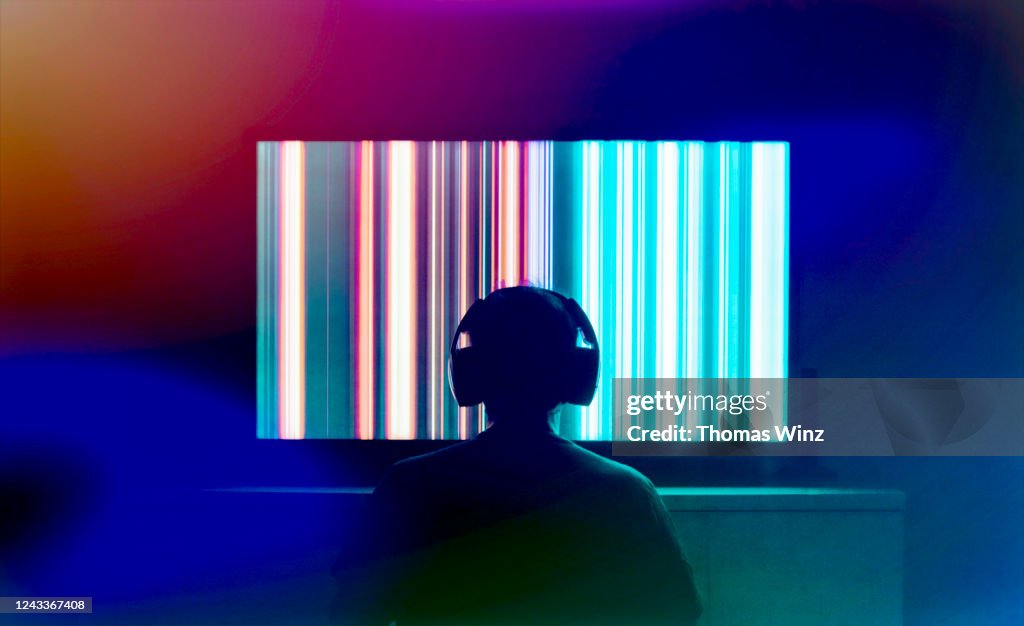 Silhouetted person with headphones watching large tv screen