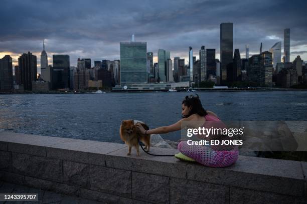 Woman sits with her dog before the east river and United Nations headquarters building amid the Mnahattan skyline, in the New York borough of Queens...