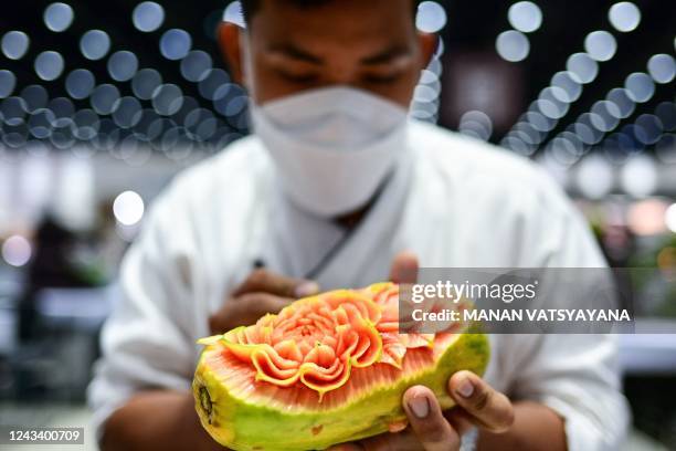 Thai participant carves patterns into a papaya during a fruit and vegetable carving competition at the 26th Thailand International Culinary Cup in...
