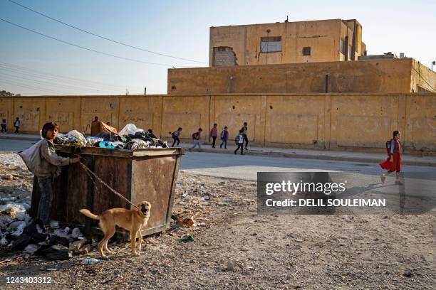 Syrian pupils walk to school as a boy salvages items from a dumpster in Syria's northern city of Raqa, on September 21, 2022.