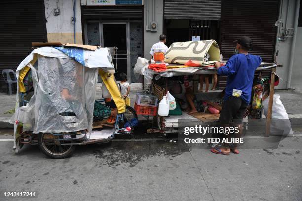 Homeless man arranges belongings on his two-wheel push cart serving as his house on wheels, as he and another homeless family inside their tricycle...