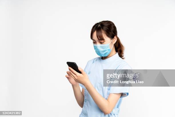 an asian woman doctor wearing a mask is using the phone - three quarter length stock pictures, royalty-free photos & images