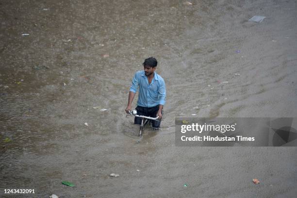 Man pulls his cycle through a waterlogged road in heavy rain on the NH-48 service road near Narsinghpur village on September 22, 2022 in Gurugram,...